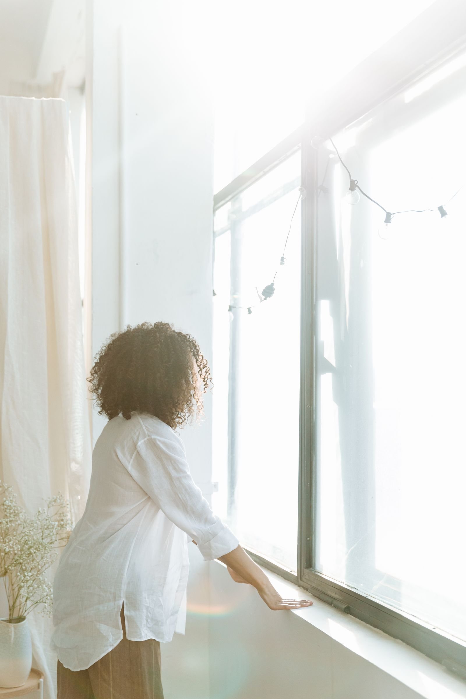Woman with curly hair standing by a sunlit window